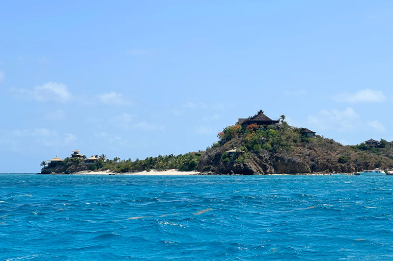 View of Necker Island from the boat during arrival, with lush greenery, shoreline, and ocean waves in the foreground