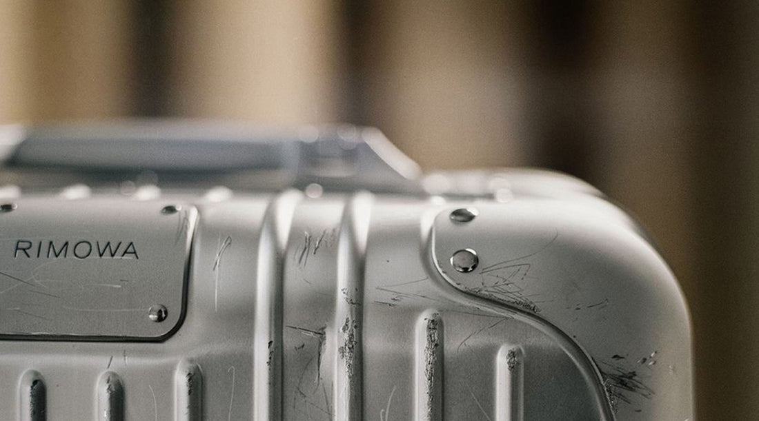lose-up of a Rimowa suitcase corner with visible scuffs—capturing the worn elegance of premium travel gear